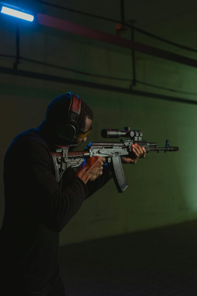 A man with ear protection using a rifle for target practice indoors.